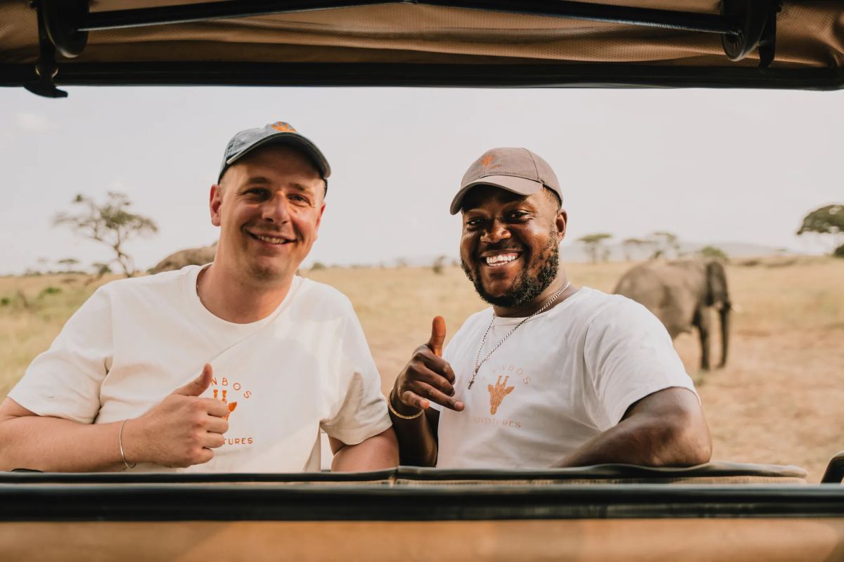 Lucas und Guide in Fynbos-Shirts im Safarifahrzeug, dahinter ein Elefant in der Serengeti