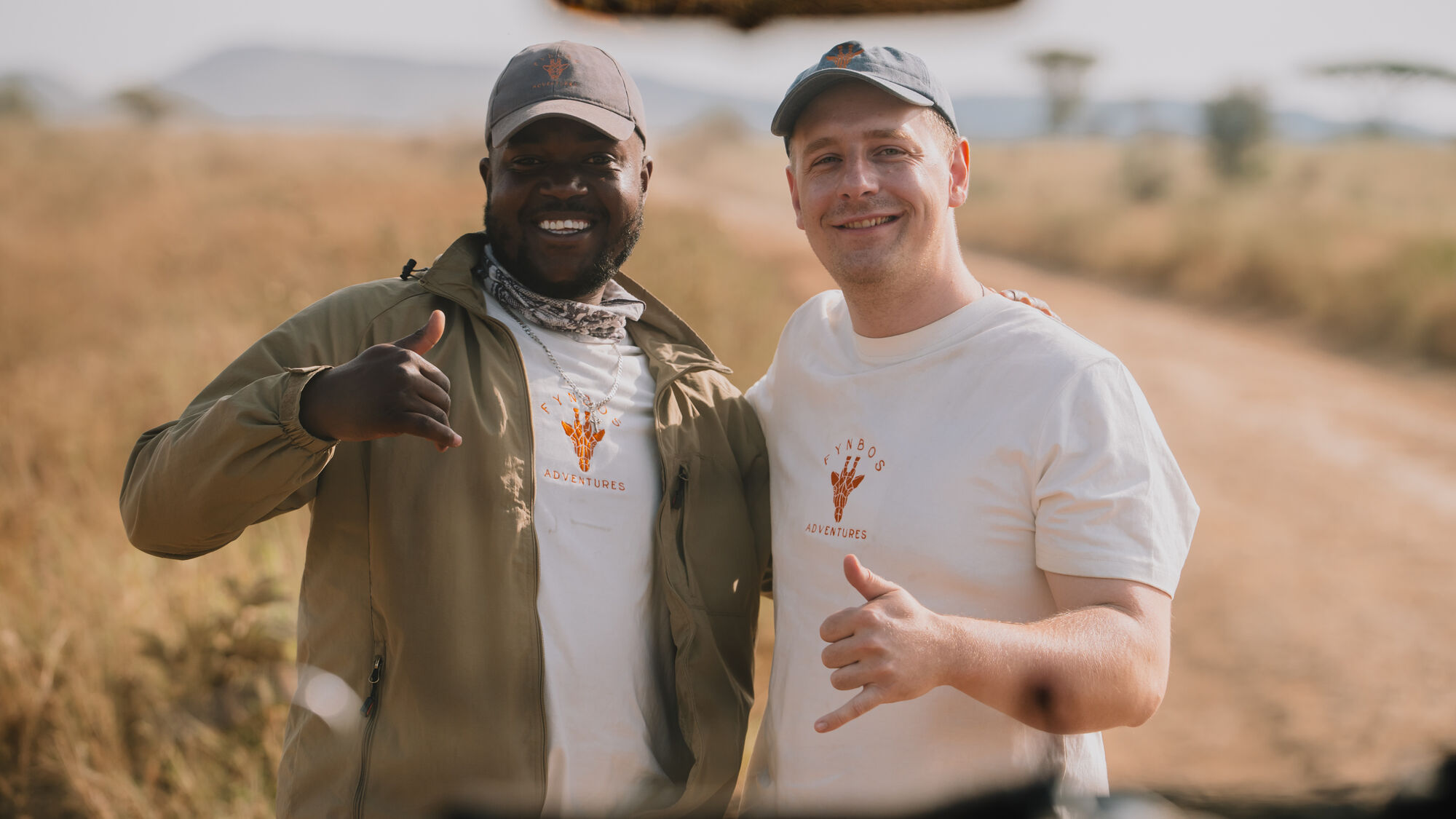Tony und Lucas lachen mit Daumen hoch in die Kamera, durch die Windschutzscheibe fotografiert